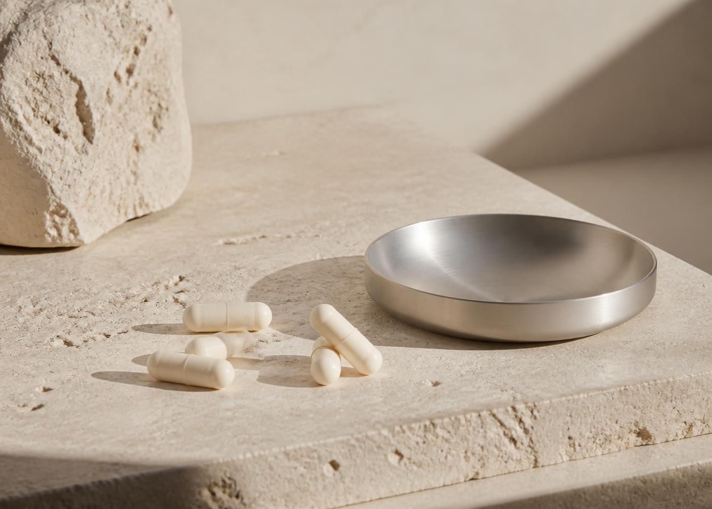 Capsules and a brushed aluminium dish on warm ivory stone